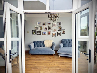Two doors open showing the inside of a room. The are two blue sofa seats. Above the seats there are 18 Linea Black frames from Frame X. Each frame has different photos from a family wedding. 