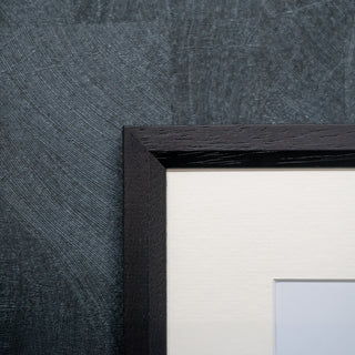Close-up of a black wood grain picture frame against a textured grey wall.