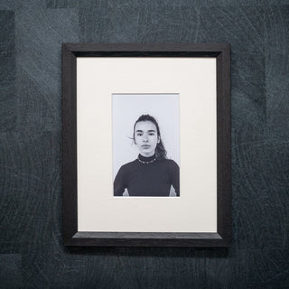 Framed black and white portrait on a textured dark wall in a black wood grain frame