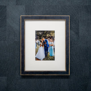 Framed photograph of a couple on their wedding day against a textured dark grey wall in a black wood frame