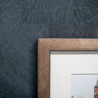 close up of the corner of a wooden bronze finished picture frame on a grey textured wall