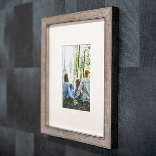 Framed photograph of a family in a forest on a textured grey wall in a wooden pewter frame.