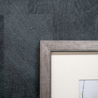 Close-up of a textured grey wall with a silver wooden picture frame.