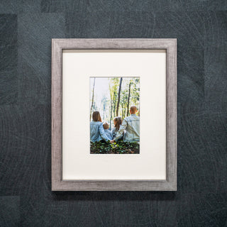 Framed photograph of a family in a forest on a textured grey wall in a silver frame