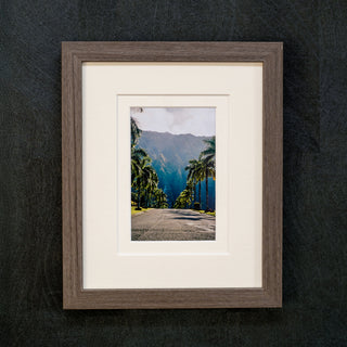 Framed photograph of a scenic road with palm trees and mountains on a dark background