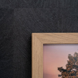 Wooden picture frame with a photo of trees against a sunset sky on a dark textured wall.