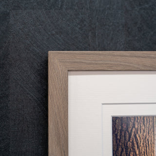 Close-up of a walnut wooden picture frame corner against a textured black wall.