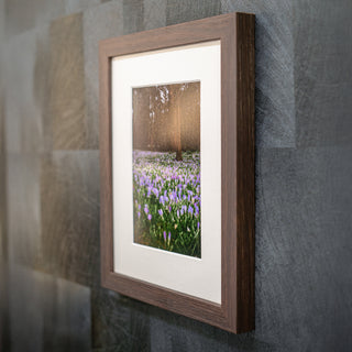 Framed photograph of a field with flowers on a textured wall dark brown wooden frame.