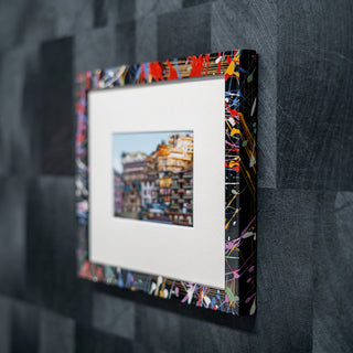 Framed artwork with a colorful abstract border on a textured gray wall.