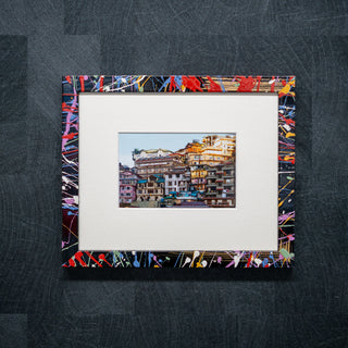 Framed photograph of a cityscape with a colorful abstract border on a textured dark surface.