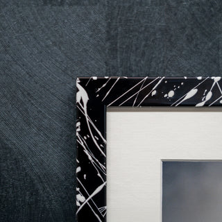 Close up of a black and white paint splatter effect picture frame on a dark wall