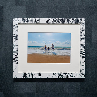 Framed photograph of a family on a beach with a black and white abstract design on the frame.