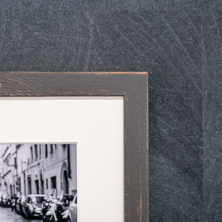 Close-up of a textured black picture frame with a blurred street scene inside.