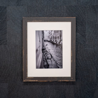 Framed black and white photo of a street scene with bicycles on a textured dark background
