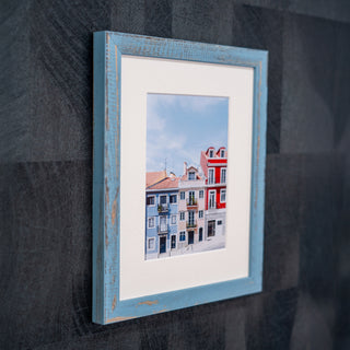 Framed picture of colourful buildings on a textured wall in a light blue wood